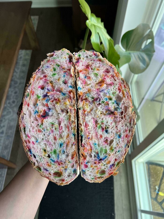 Rebanada de pan con toques de colores vibrantes sostenida en mano frente a plantas y ventana, ejemplos de terribles mentirosos.