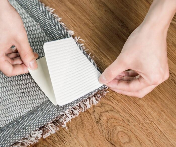 Hands applying adhesive carpet tape to a rug corner on a wooden floor, popular trending product in the Pandaverse.