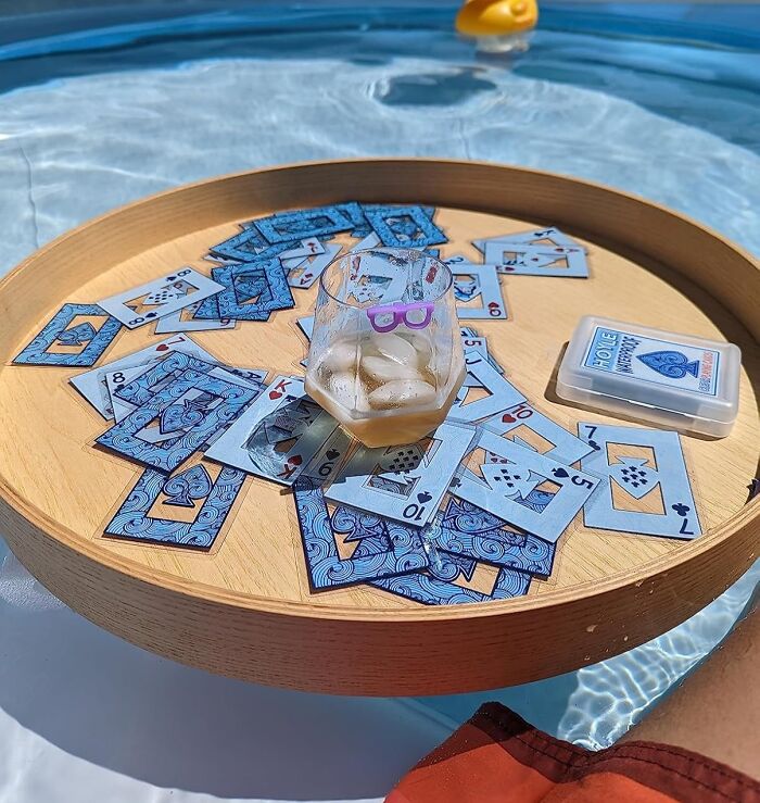 Playing floating card games with a glass of iced drink on a wooden tray, showcasing trending Pandaverse products by the pool.