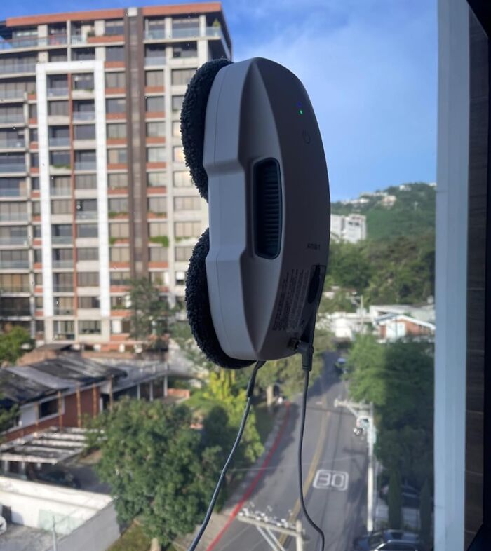 Automatic window cleaning robot attached to a glass pane with a cityscape in the background, showcasing novelty finds.