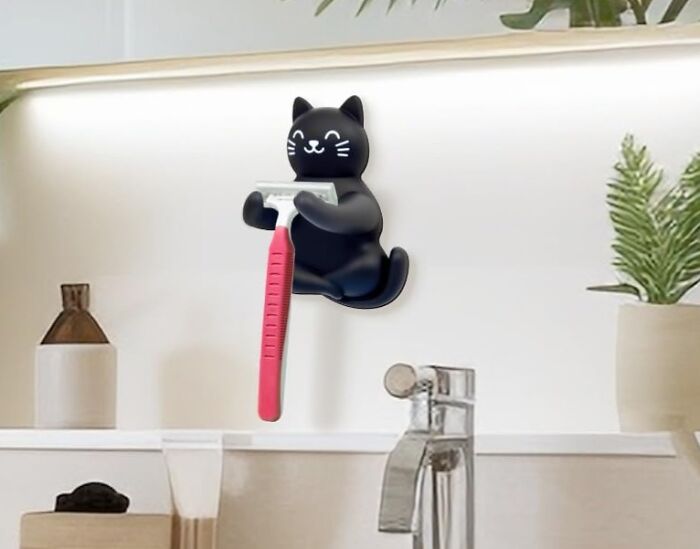 Black cat-shaped razor holder mounted on bathroom wall, a low-key genius novelty find for organizing razors.