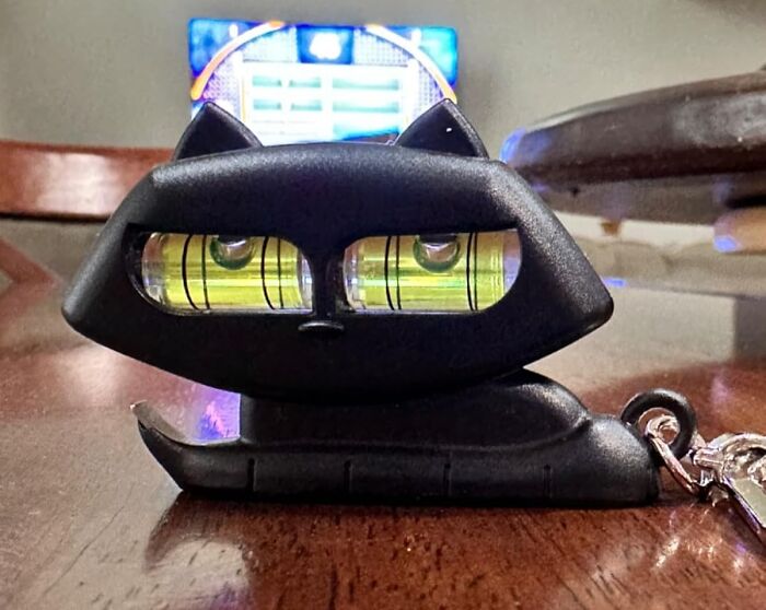 Black cat-shaped novelty level tool with bubble vials for accurate measurements on a wooden table surface.