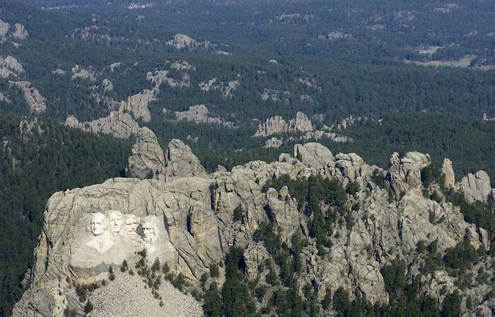 Aerial view of Mount Rushmore showing famous landmarks from unexpected angles with surrounding forest and rocky terrain.