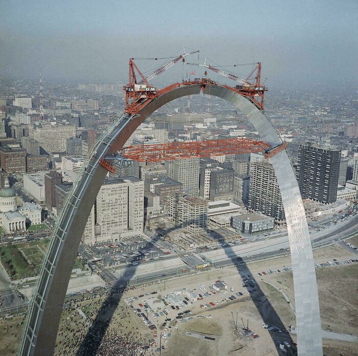 Construction cranes working on the arch of a famous landmark, showcasing an unexpected angle and unique perspective.