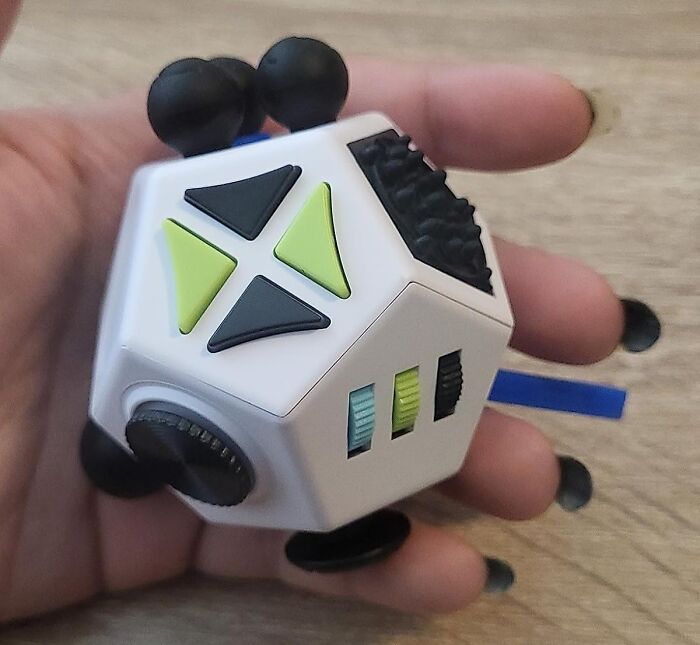 Person holding a multi-sided fidget toy with buttons and switches, ideal for keeping a 12-year-old entertained.