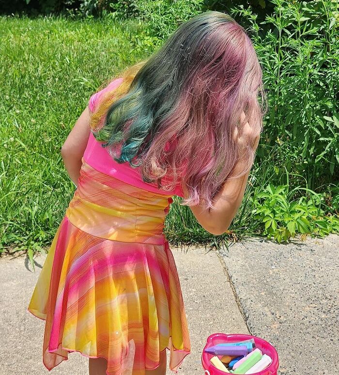 Young girl with colorful hair and dress outdoors, holding chalk, representing shopping for a 12-year-old gift ideas.