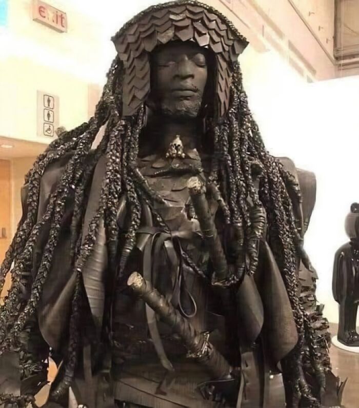 Dark bronze sculpture resembling a warrior with braided hair and armor, representing an artifact in the archaeology world.