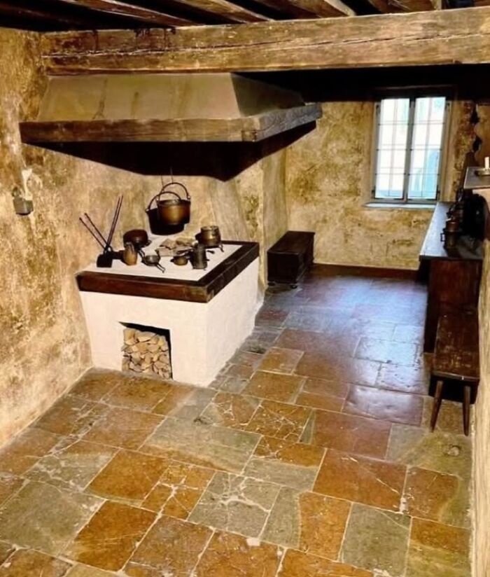 Rustic historical kitchen interior with stone floor, wooden beams, and vintage cooking utensils in archaeology world setting.