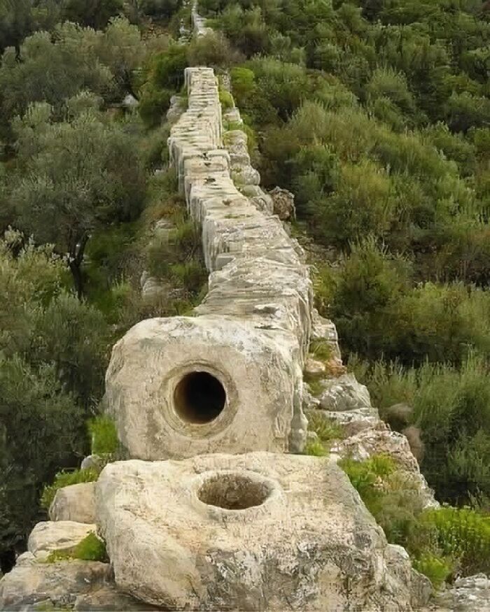 Ancient stone aqueduct ruins in a green hilly landscape showcasing archaeology world historical remains.