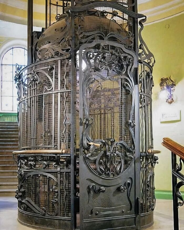 Ornate historical wrought iron elevator cage inside a vintage building, showcasing intricate metalwork details in archaeology world.