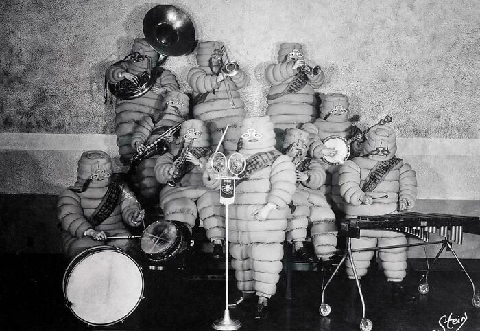 Vintage band dressed in unusual padded costumes performing with instruments in a ridiculous pic from the past.