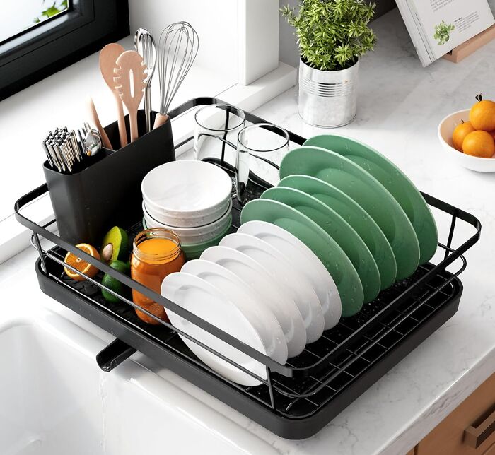 Black dish rack with green and white plates, utensils, and glasses drying on a kitchen countertop for kitchen Prime Day wishlist.