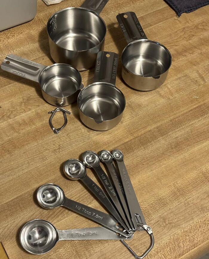 Stainless steel measuring cups and spoons on a wooden countertop, essential kitchen tools for precise cooking.