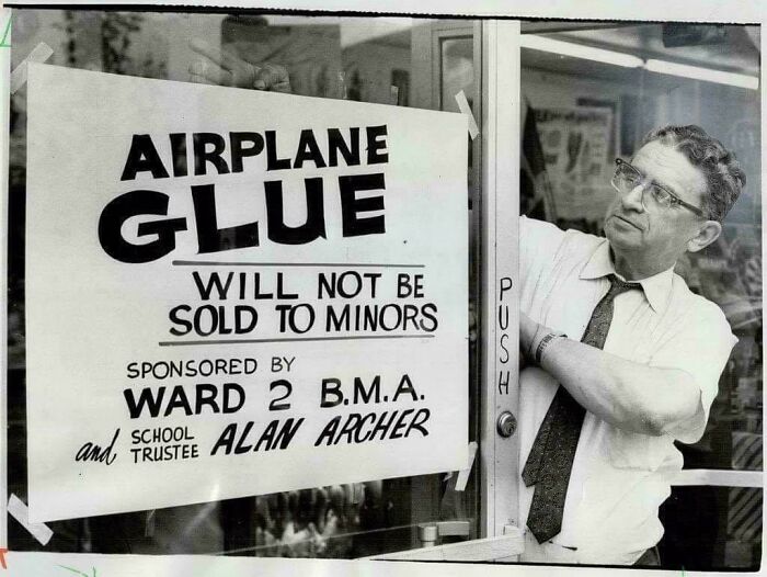 Man taping a vintage sign about airplane glue restrictions, reflecting past regulations that would not fly today.