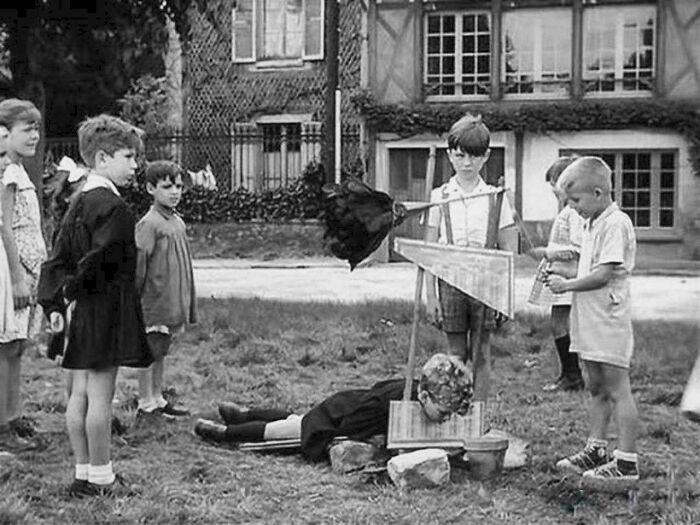 Group of children in a bizarre game with a contraption outdoors, a ridiculous pic from the past that would never fly today