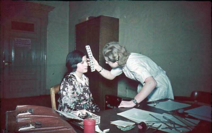 Woman in floral dress receiving an eye exam from medical professional in a vintage setting, ridiculous pics from the past.