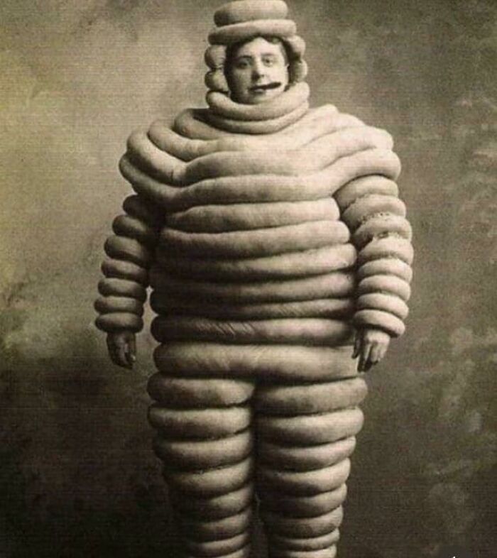 Vintage black and white photo of a man wearing a bizarre suit made of stacked circular tubes, a ridiculous pic from the past.