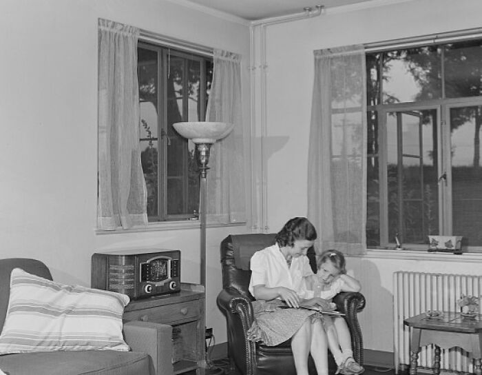 1940s housewife reading a book with her daughter in a cozy living room, capturing iconic moments of home life.