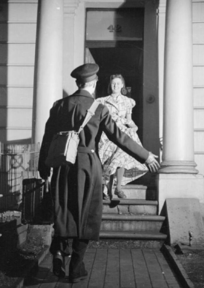 1940s housewife warmly greeting a returning soldier at the doorstep during wartime in a black and white photo.