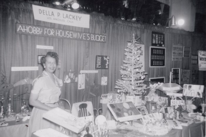 1940s housewife smiling at a craft booth displaying homemade decorations and gifts during a festive event