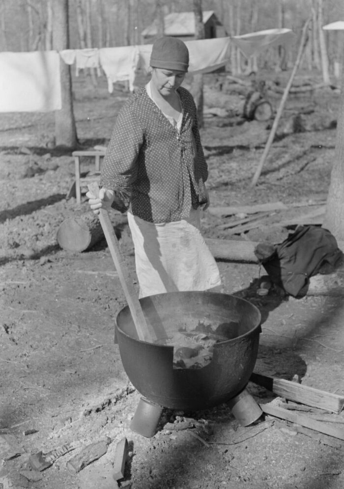 1940s housewife stirring large pot outdoors near clothesline in a rural setting during daily chores.