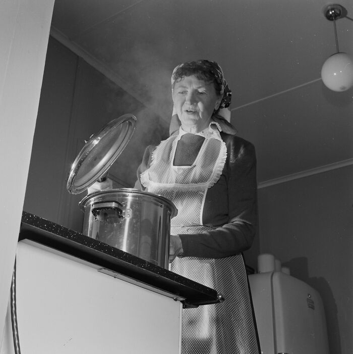 1940s housewife cooking at stove wearing apron and headscarf, steam rising from pot in vintage kitchen setting