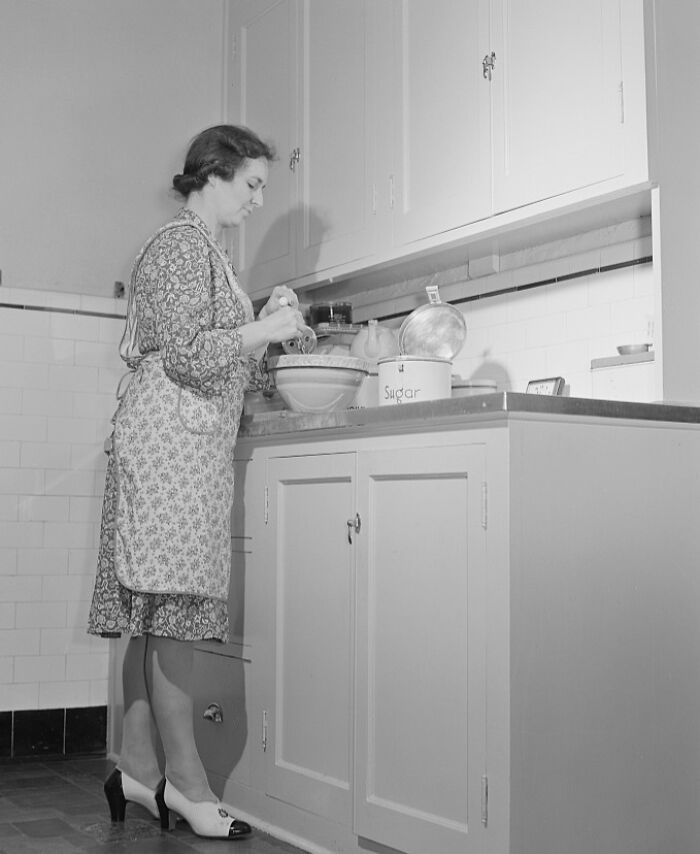 1940s housewife in apron mixing ingredients in kitchen, representing iconic photos of 1940s housewives at home.