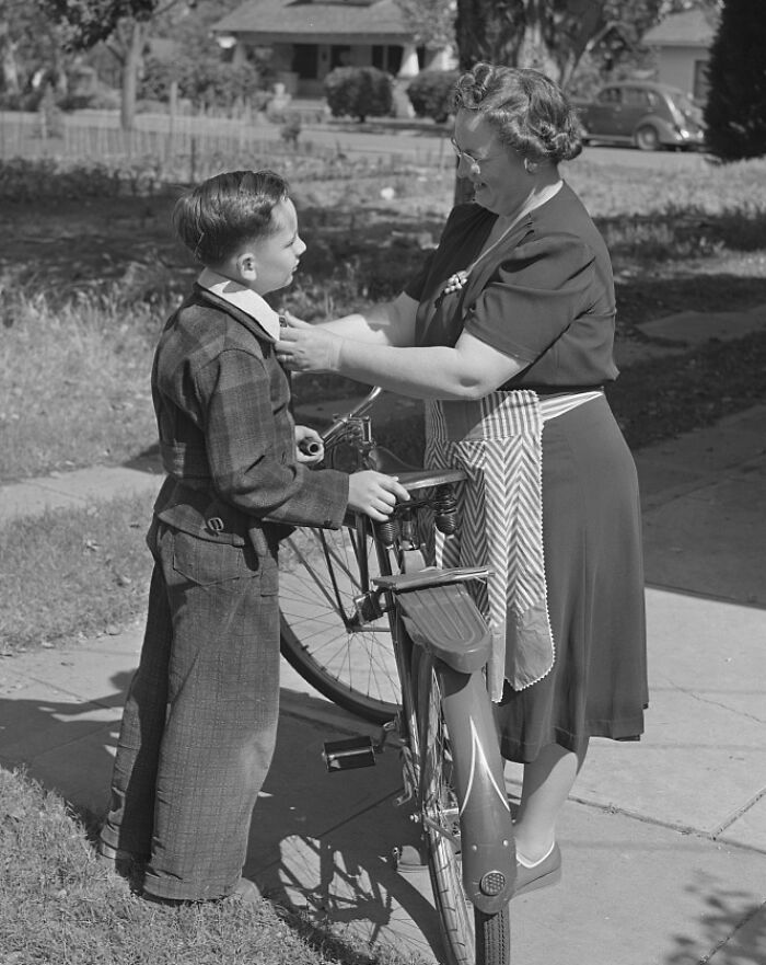 1940s housewife helping her son by a bicycle outside a suburban home, showcasing iconic housewife moments.