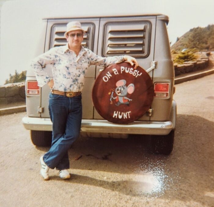 Man in vintage outfit leaning against van with humorous spare tire cover, a ridiculous pic from the past that would never fly today