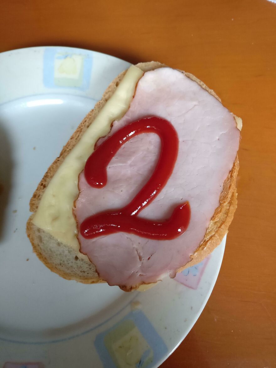 Sandwich with ham and cheese on a plate featuring the number two written in ketchup, a perfect handwriting example.