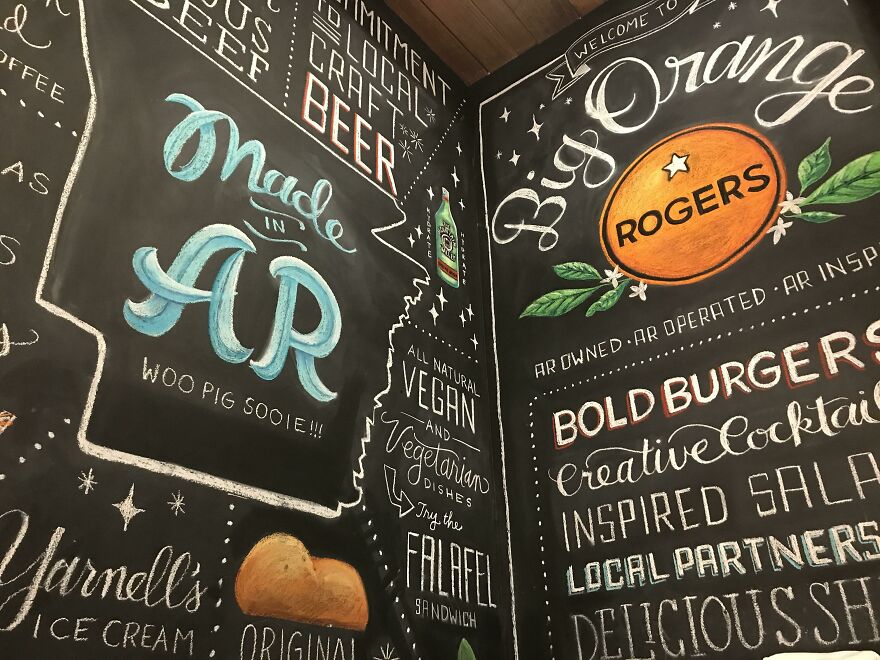 Chalkboard wall art showcasing perfect handwriting examples with creative fonts and colorful illustrations in a restaurant setting.