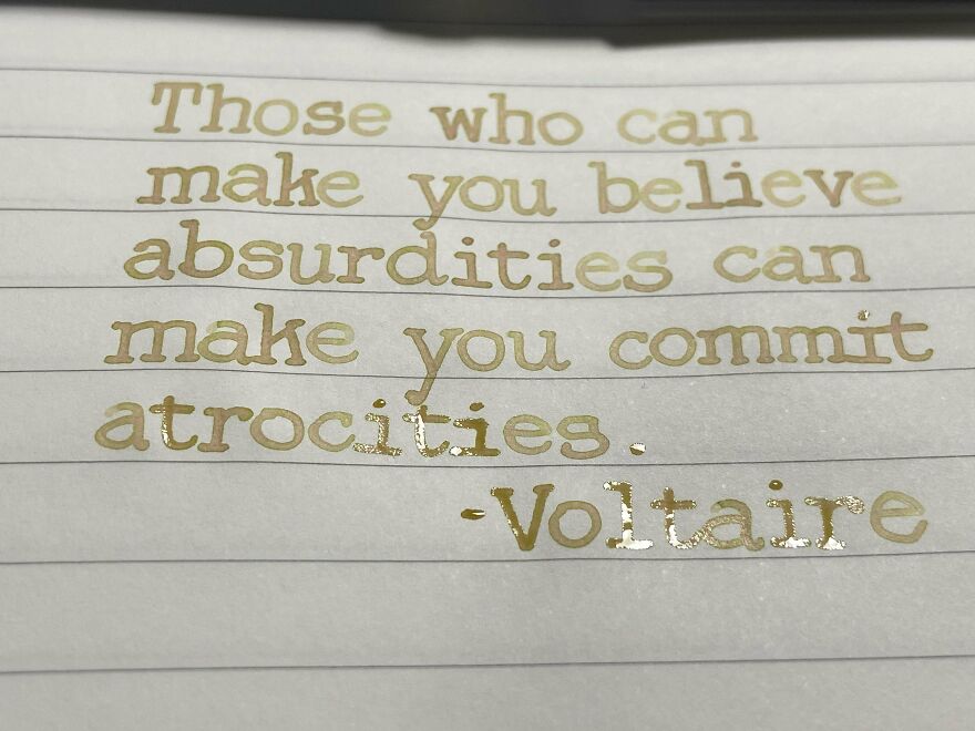 Handwriting example of a Voltaire quote written neatly in gold ink on lined paper, showcasing perfect handwriting.