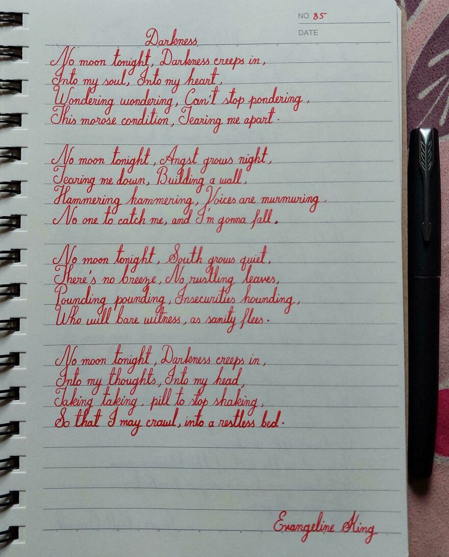 Neatly written poem in red ink showcasing perfect handwriting examples on a lined notebook page with a black pen beside it.