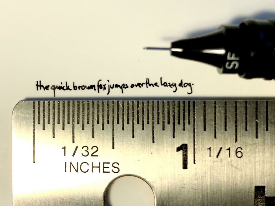 Extremely small perfect handwriting example of the phrase written with a fine pen above a metal ruler.