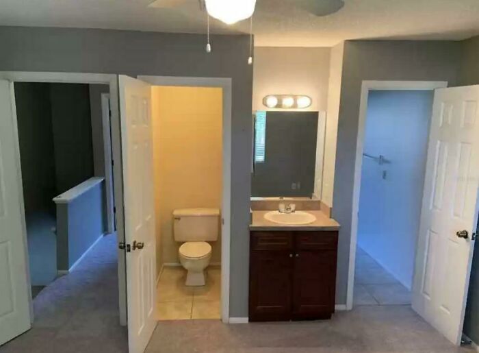 Unhinged real estate listing showing a bathroom with toilet, sink, and multiple open doors in a poorly designed layout.
