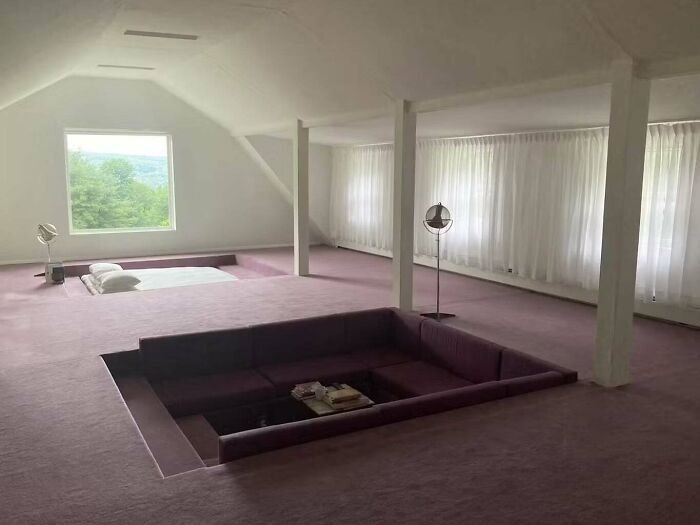 Spacious room with a sunken purple couch and bed area, showcasing unhinged real estate listing design choices.