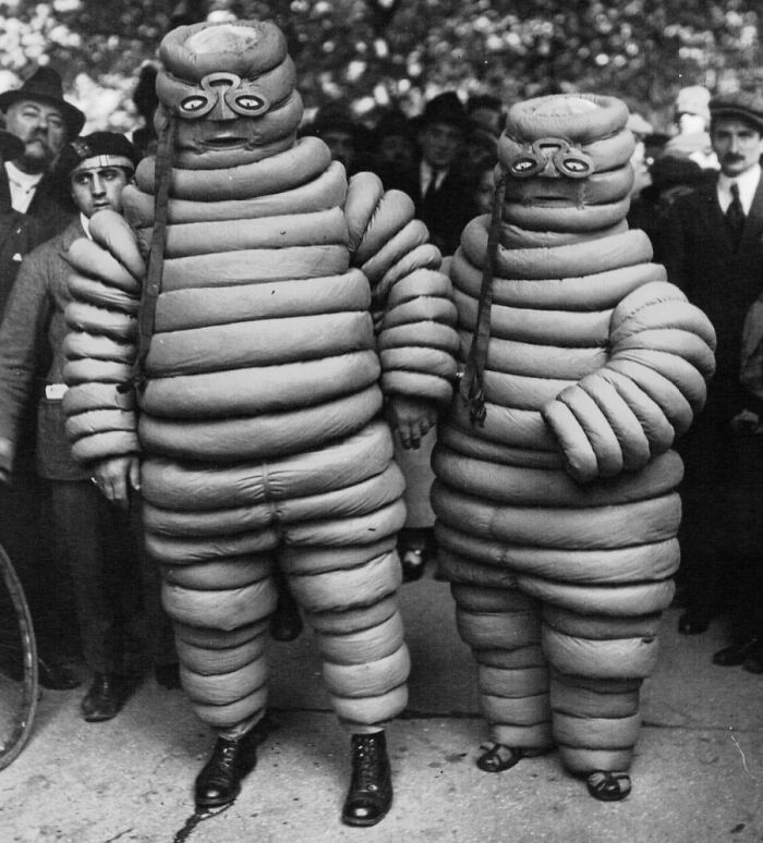 Two people in vintage, creepy Michelin Man-like costumes posing outdoors, unsettling photo from the past.