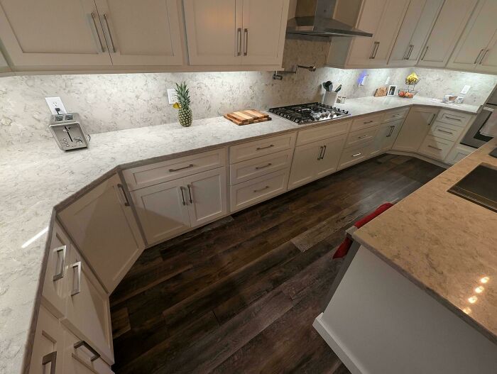 Modern kitchen with white cabinets and marble countertops showing a hilarious partner fail with misplaced cabinet handles.