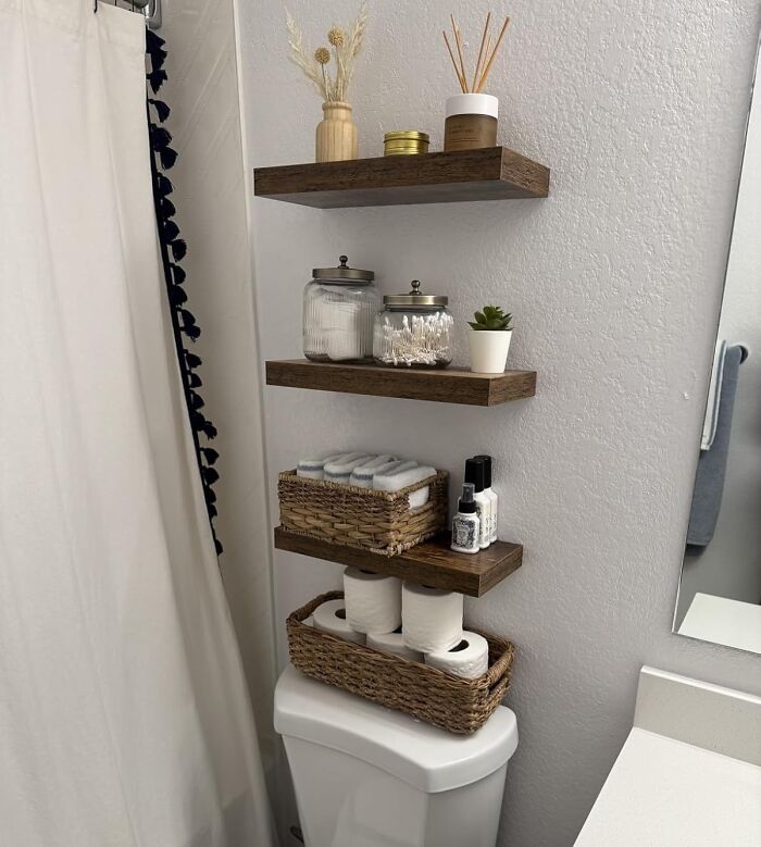 Floating wooden shelves in a bathroom holding home organization items in a neat and stylish home deals setup.