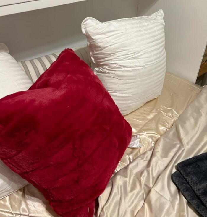 Red plush pillow and white pillow arranged on a bed with beige satin sheets highlighting Prime Day home deals.