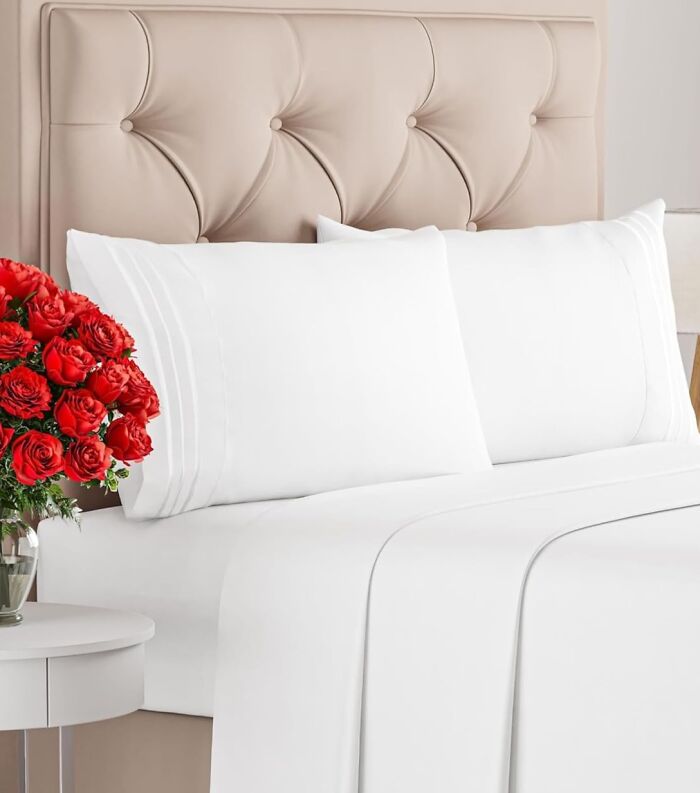 White bed sheets and pillowcases on a beige tufted headboard with a vase of red roses on a side table prime day home deals