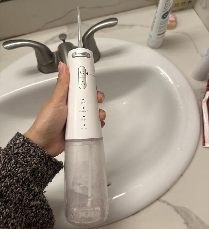 Hand holding a white water flosser over a bathroom sink, showcasing Prime Day deals under $25 safe for your bank account.