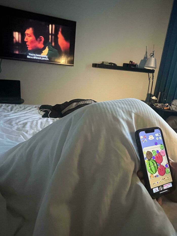 Person hiding under a blanket while playing a mobile game, showcasing hilarious clueless partners moments at home.