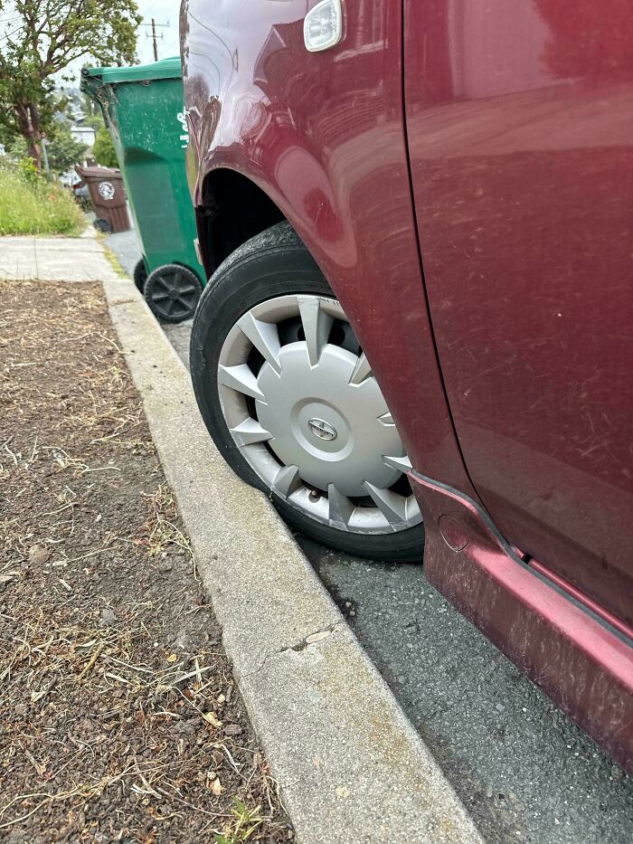 Flat tire on a maroon car parked next to a curb, illustrating clueless partner parking fail in hilarious photos.