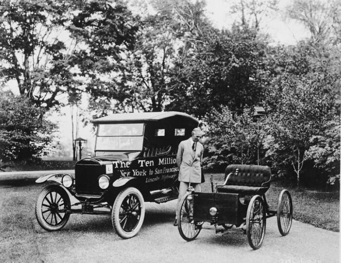 Early 20th century historical photo showing two vintage automobiles and a man standing outdoors near trees.