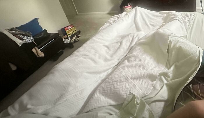 A bed covered with a large white blanket humorously hiding a person, showcasing clueless partner moments.