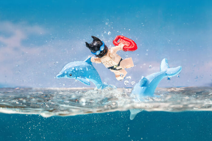 LEGO figure wearing a cat mask and goggles jumping from water with two LEGO dolphins in a dynamic scene.