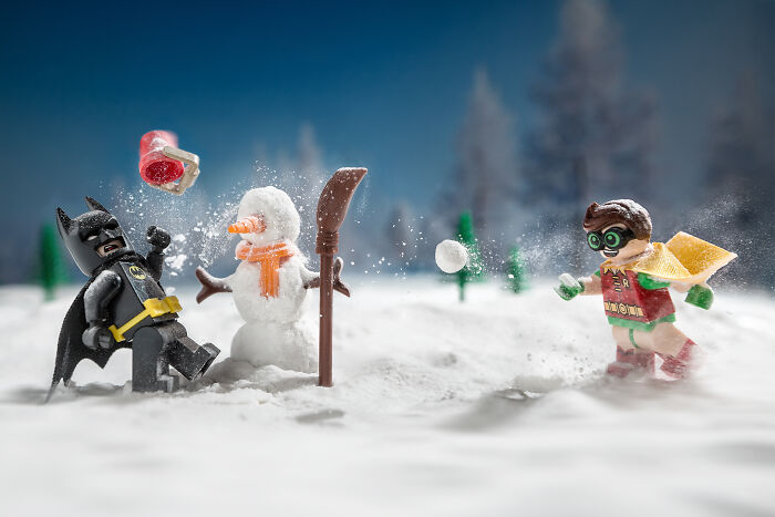 LEGO figures of Batman and Robin engaged in a snowy snowball fight scene with a snowman in a detailed diorama.