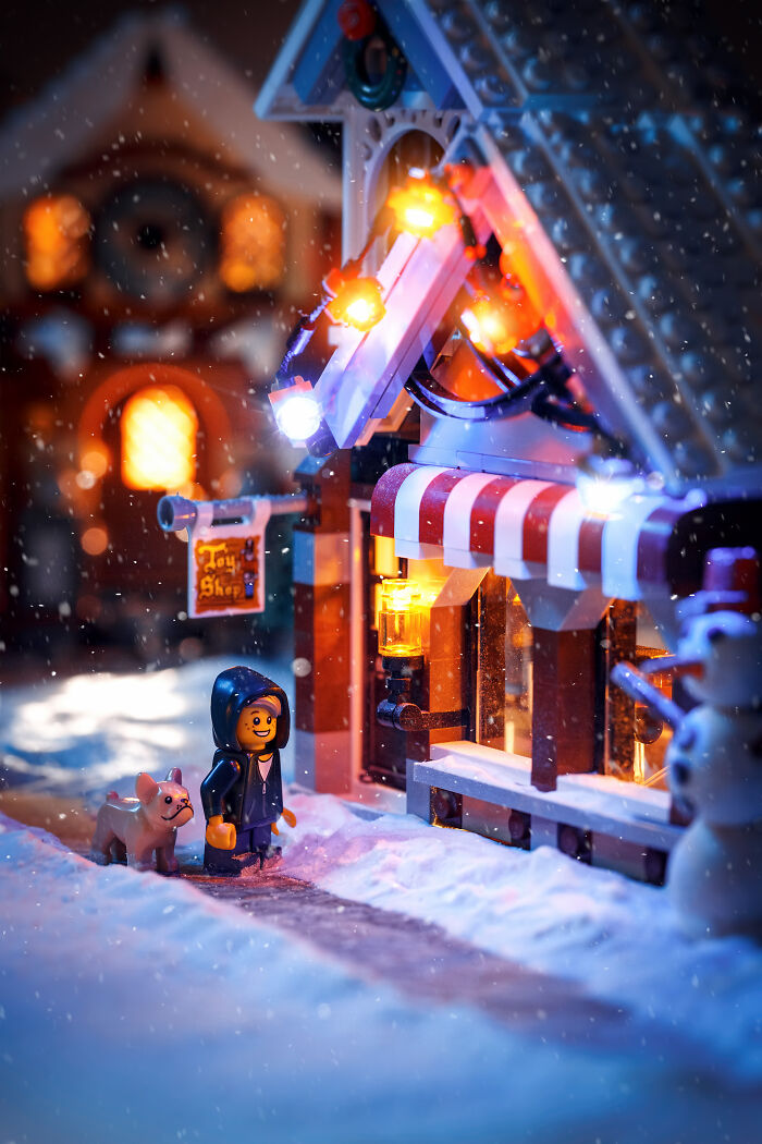 LEGO scene of a snowy toy shop with glowing lights and a minifigure walking a dog in the winter night.