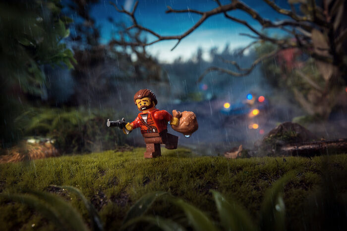 LEGO figure in detailed outdoor scene holding a bag and gun, showcasing Hollywood-level photography with dramatic rain effects.